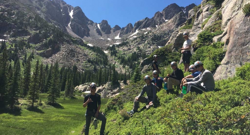 A group of people rest in green grass, surrounded by mountains. 